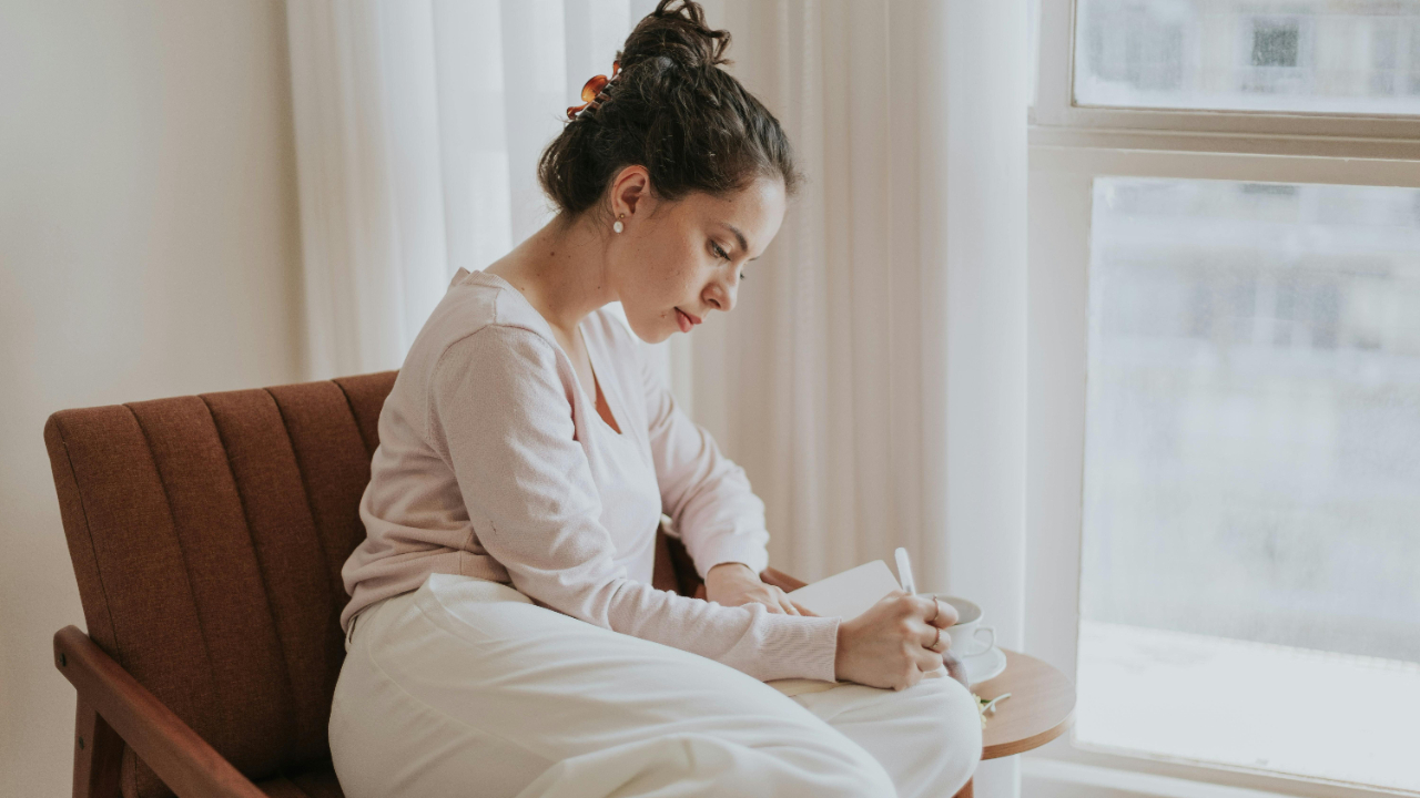 Woman journaling quietly by a window, reflecting on faith and finances in a calm moment
