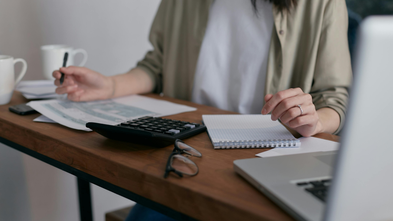 Woman sitting at a desk with a notebook, pen, and financial papers, calmly reviewing her finances without using a budgeting app