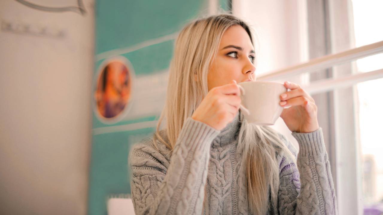 Woman holding a coffee cup and looking out a window, representing hope and a fresh financial start
