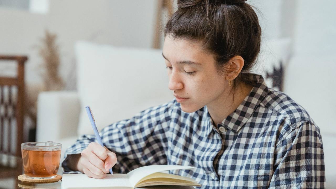 woman journaling in a quiet home setting with a cup of tea, reflecting calmly without pressure