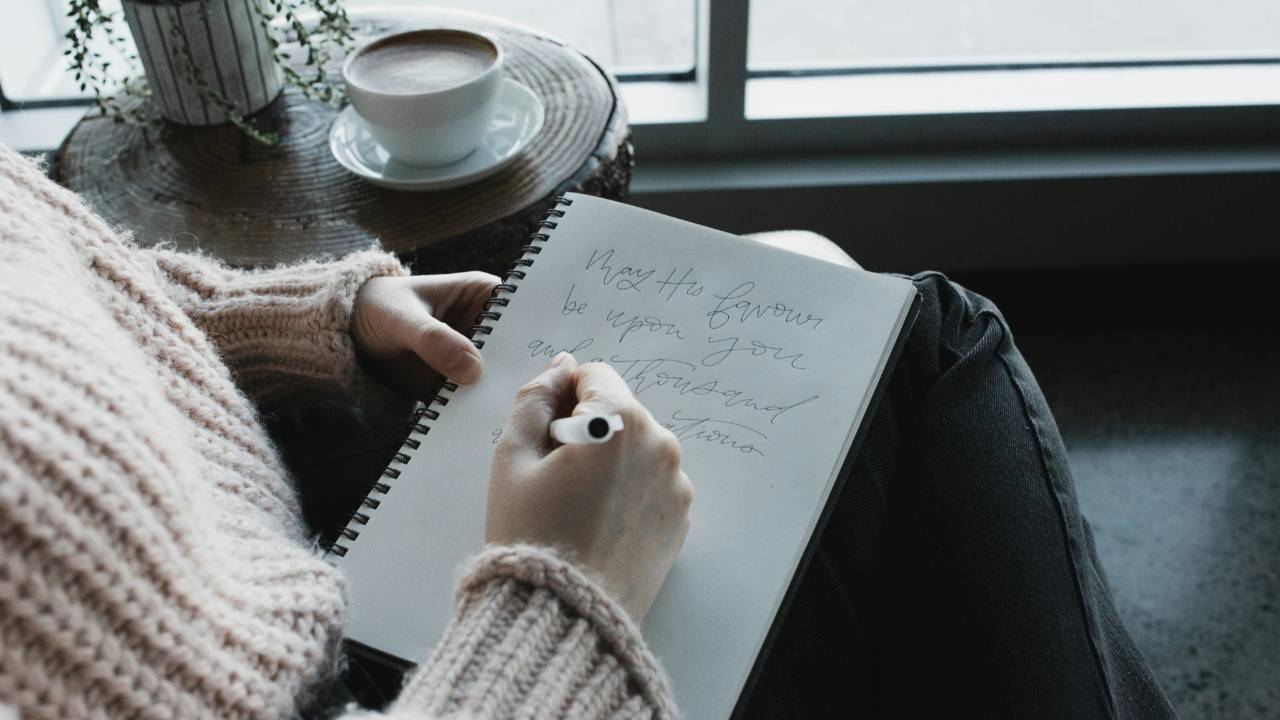 Woman journaling by a window with coffee, reflecting calmly as she rebuilds trust and confidence with money