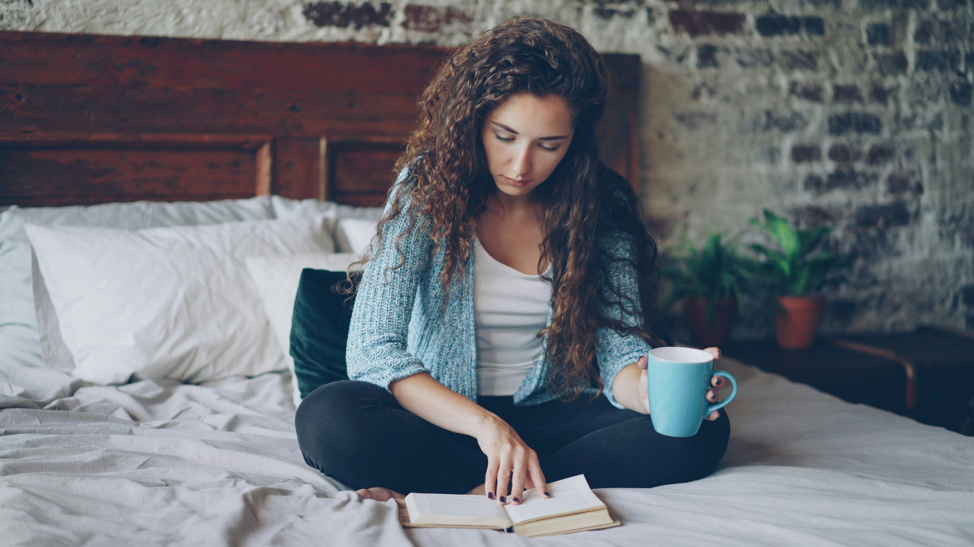Woman sitting on her bed with a cup of coffee and an open journal, reflecting quietly during a financial rebuild.