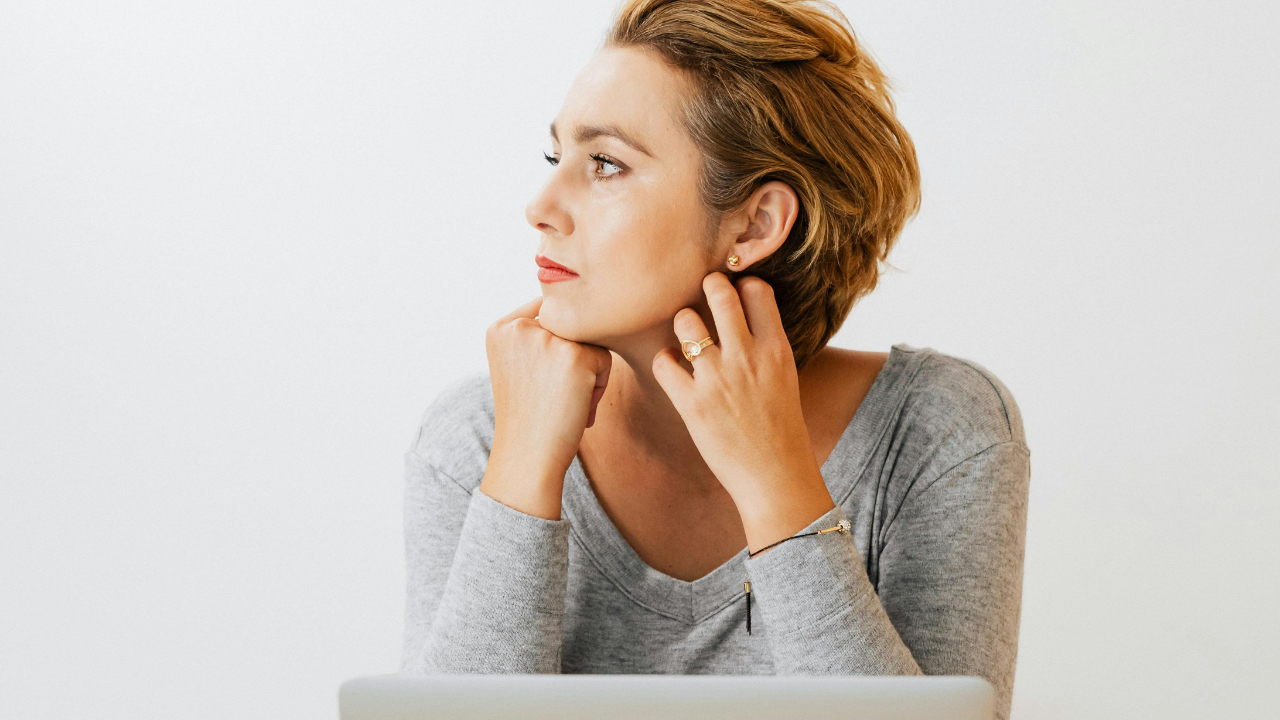 A woman sitting at a desk with a laptop, looking thoughtful and calm as she reflects on rebuilding her credit without shame.