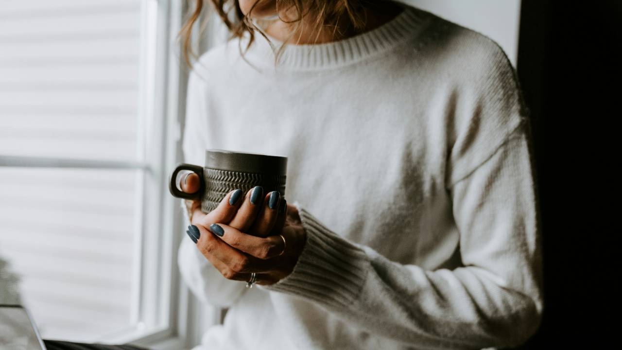 Woman holding a cup of coffee by a window during a calm, reflective moment about understanding her debt without shame