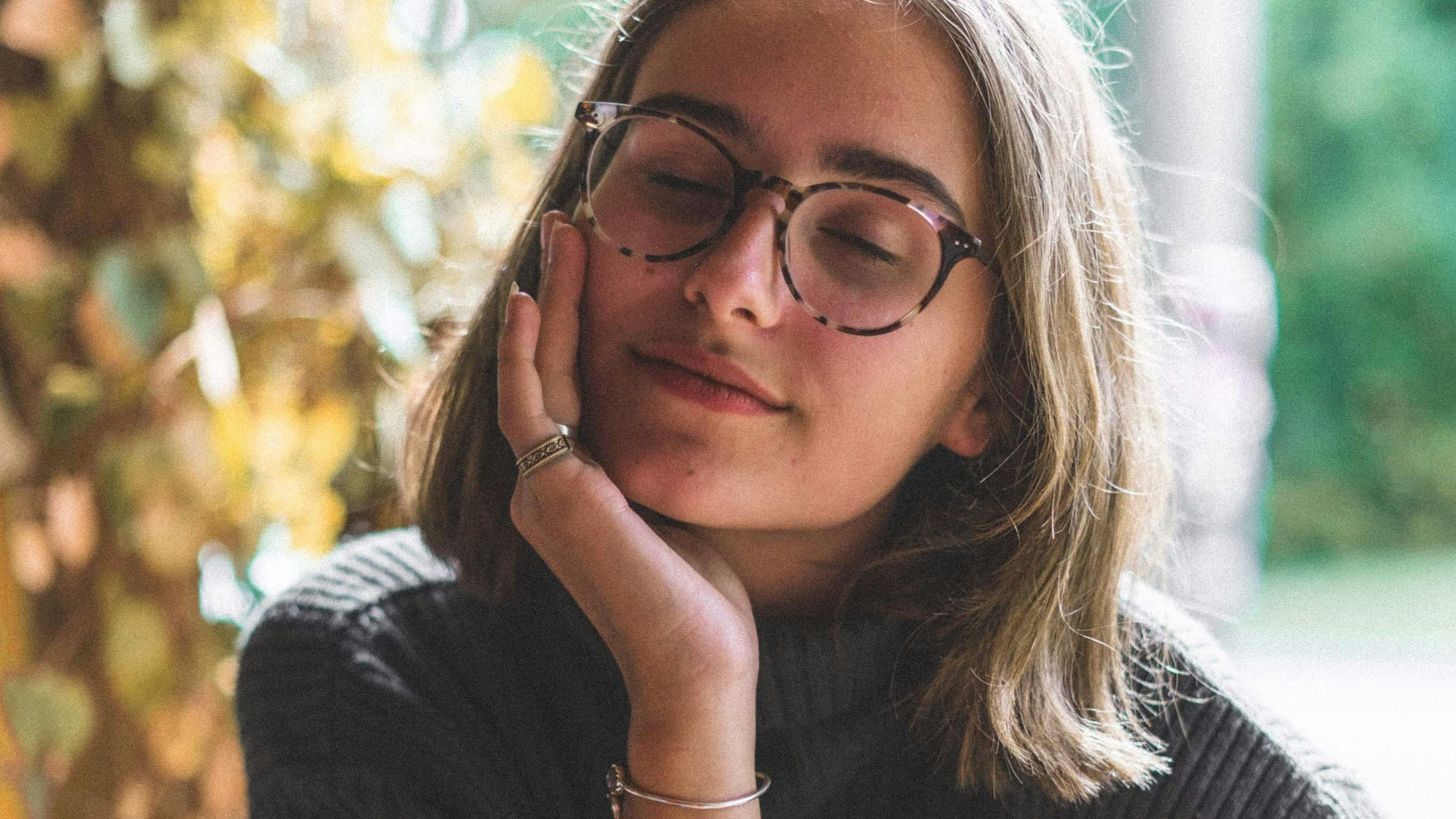 A woman sitting calmly with a cup of coffee, eyes closed, enjoying a quiet moment of peace and reflection.