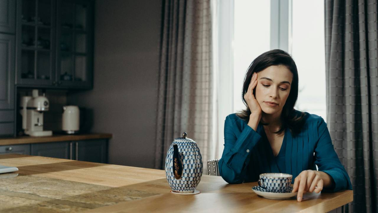 Single mom sitting at a kitchen table with coffee, quietly reflecting on money and responsibility