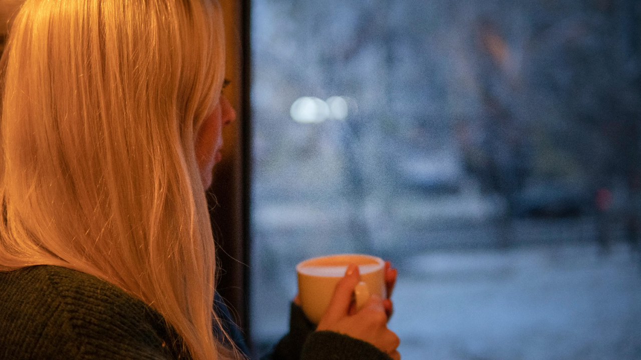 Woman holding a coffee mug and looking out a window, reflecting on starting over financially.