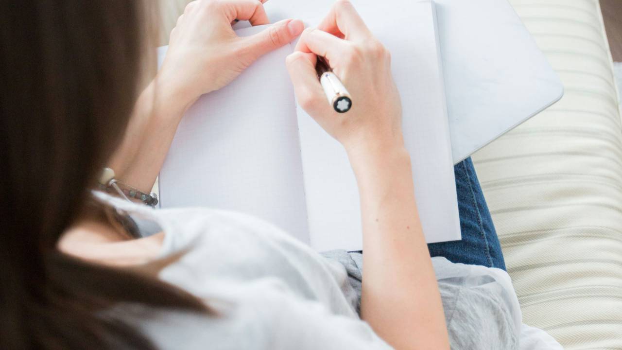 A woman sitting on a couch writing in a notebook, representing small steps toward financial stability and calm.