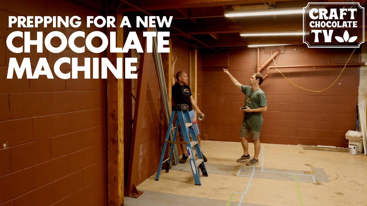 Image of two men renovating a chocolate factory with text reading "Prepping For A New Chocolate Machine". 