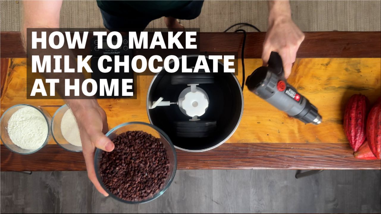 Image of hands pouring cacao nibs into grinder with text reading "How To Make Milk Chocolate At Home". 