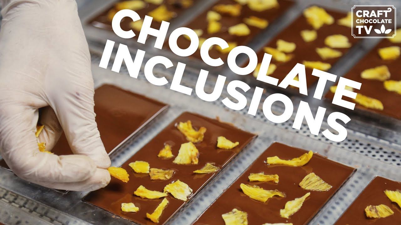 Image of a hand adding flower leafs to a chocolate bar with text reading "Chocolate Inclusions". 