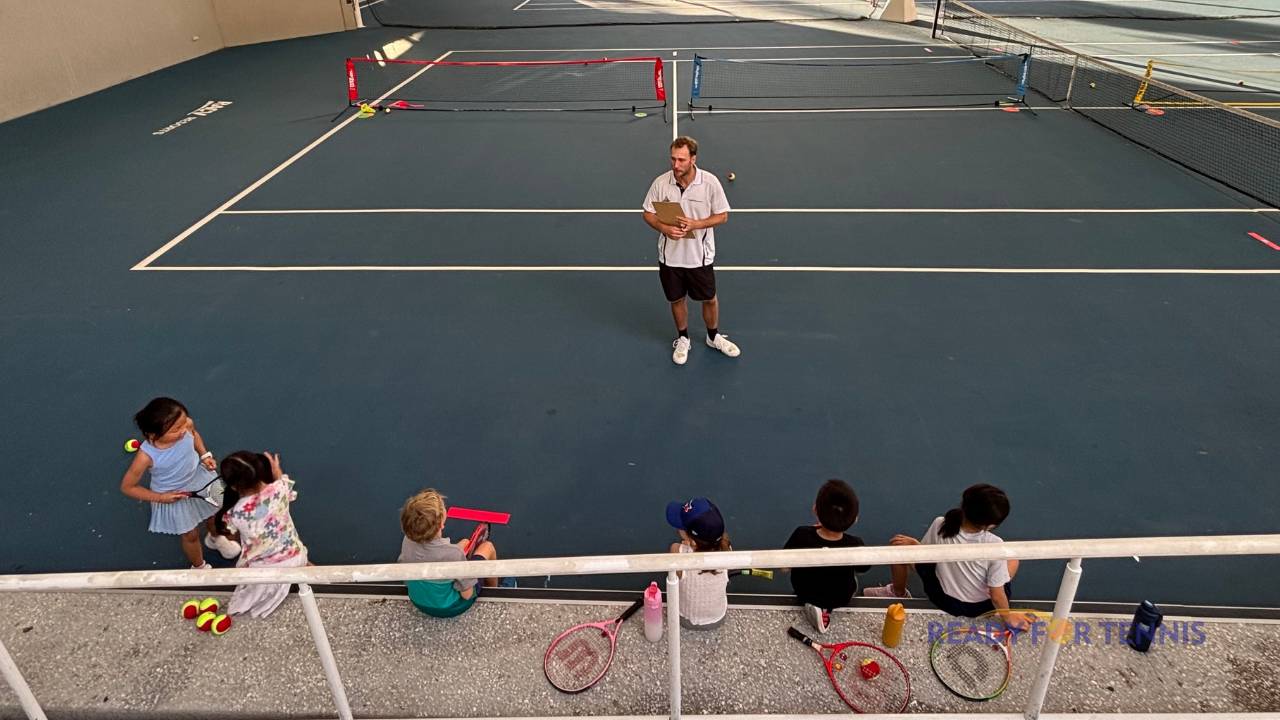 A Ready for Tennis coach guiding young players during a Red Ball and Orange Ball Matchplay session, with kids listening courtside at RACV Royal Pines.