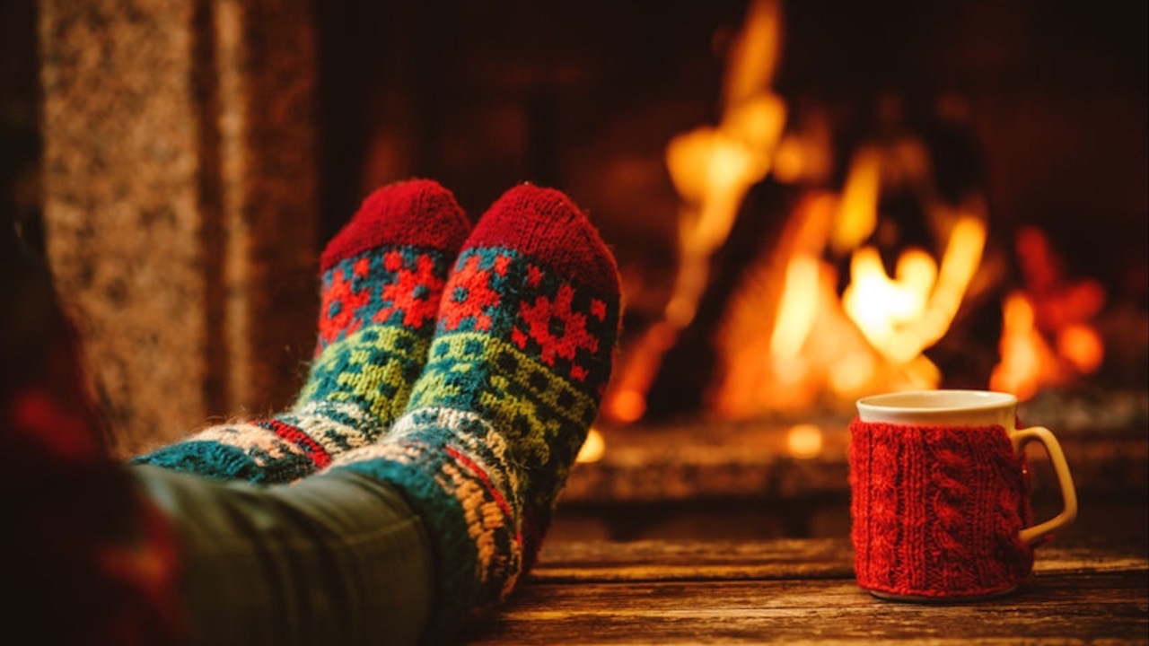 Person sitting in front of a fireplace with a hot beverage, reflecting and pausing for a year-end life reset and intentional living.
