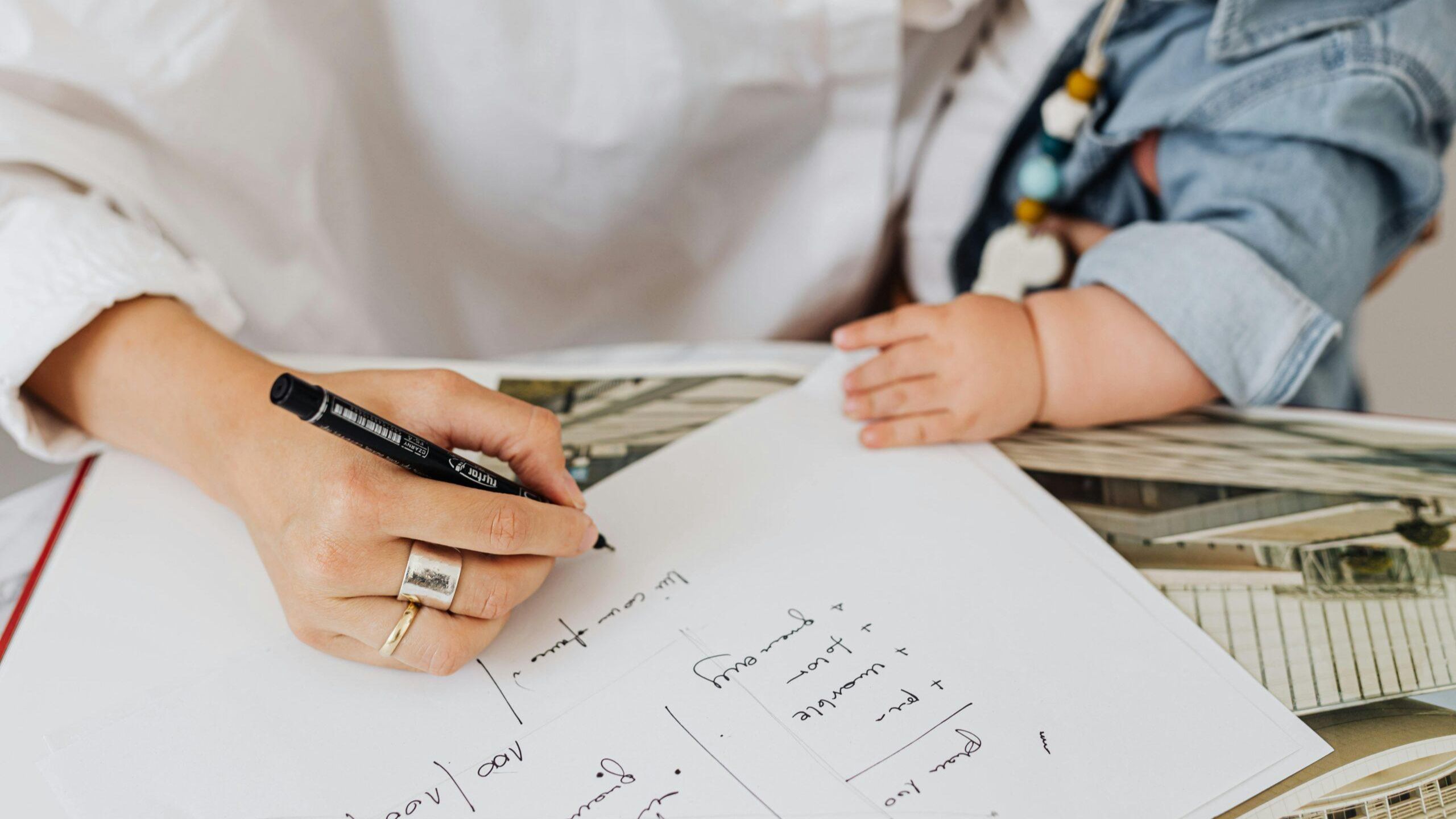 mother-writing-notes-while-holding-baby