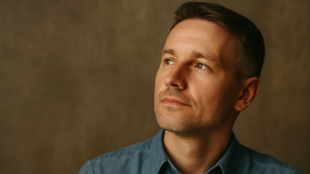 Thoughtful man in a blue denim shirt gazing upward and to the right, set against a warm, textured background, symbolizing reflection and introspection.