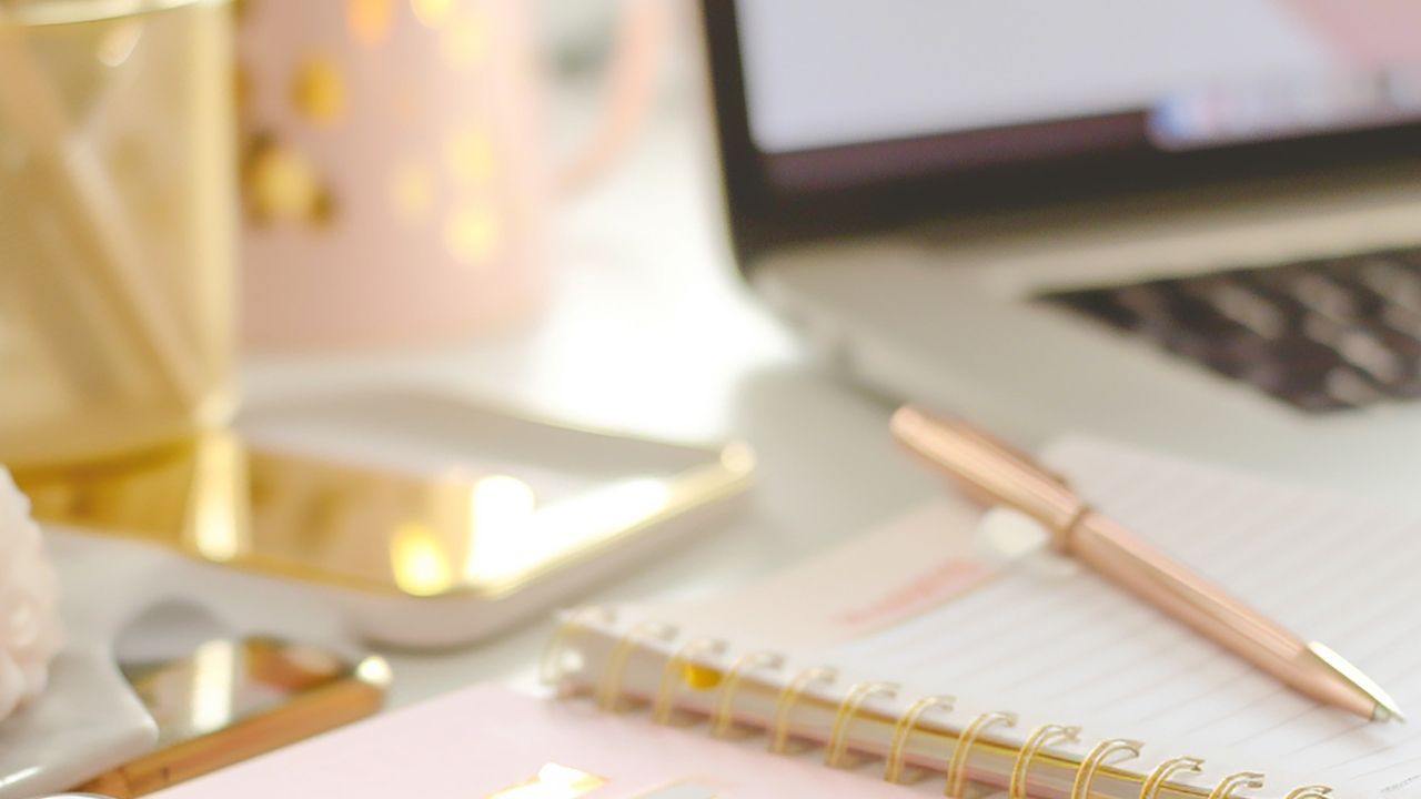 Soft, neutral workspace with a notebook, pen, laptop, and warm light on a desk.