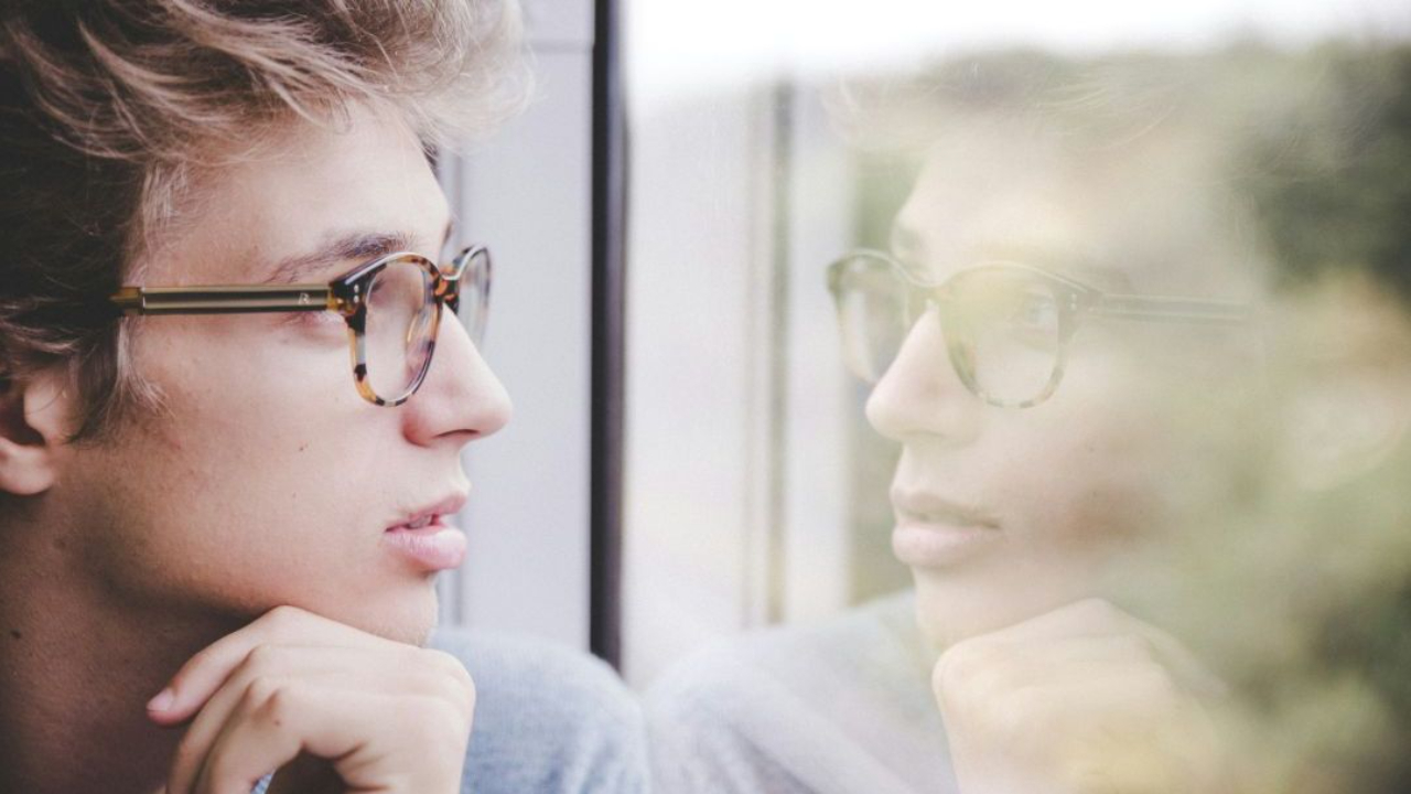 man looking out window with self image