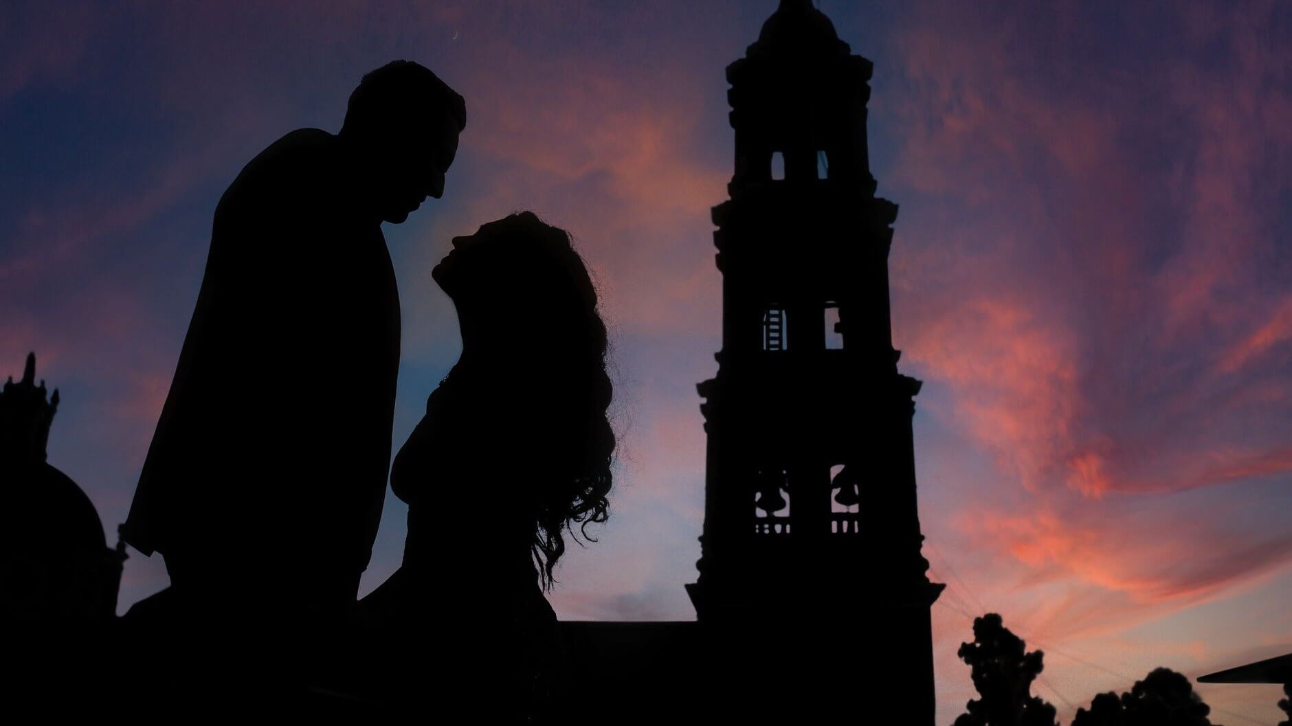 silhoutte of a man and woman holding hands in front of a church