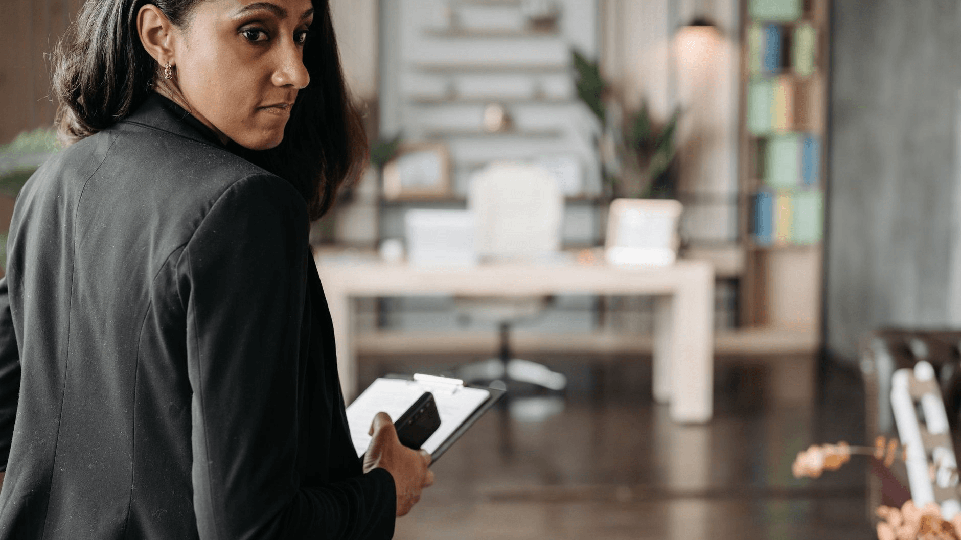 a woman in dark clothing holding a phone looking back