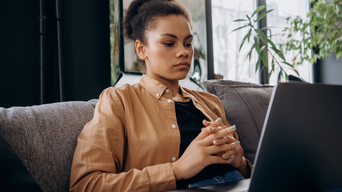 Woman seated thoughtfully beside a laptop, considering whether a money mindset course is right for her