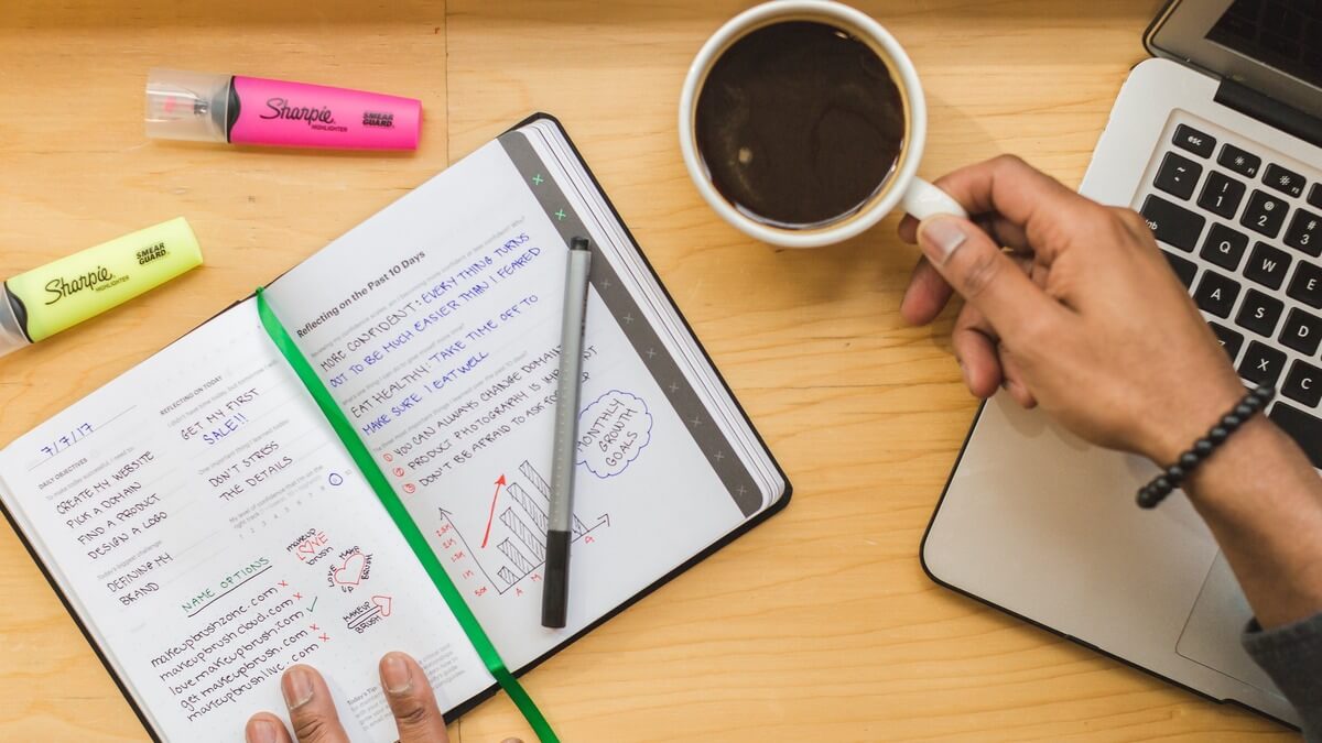a work table with notebook, ballpen, and coffee