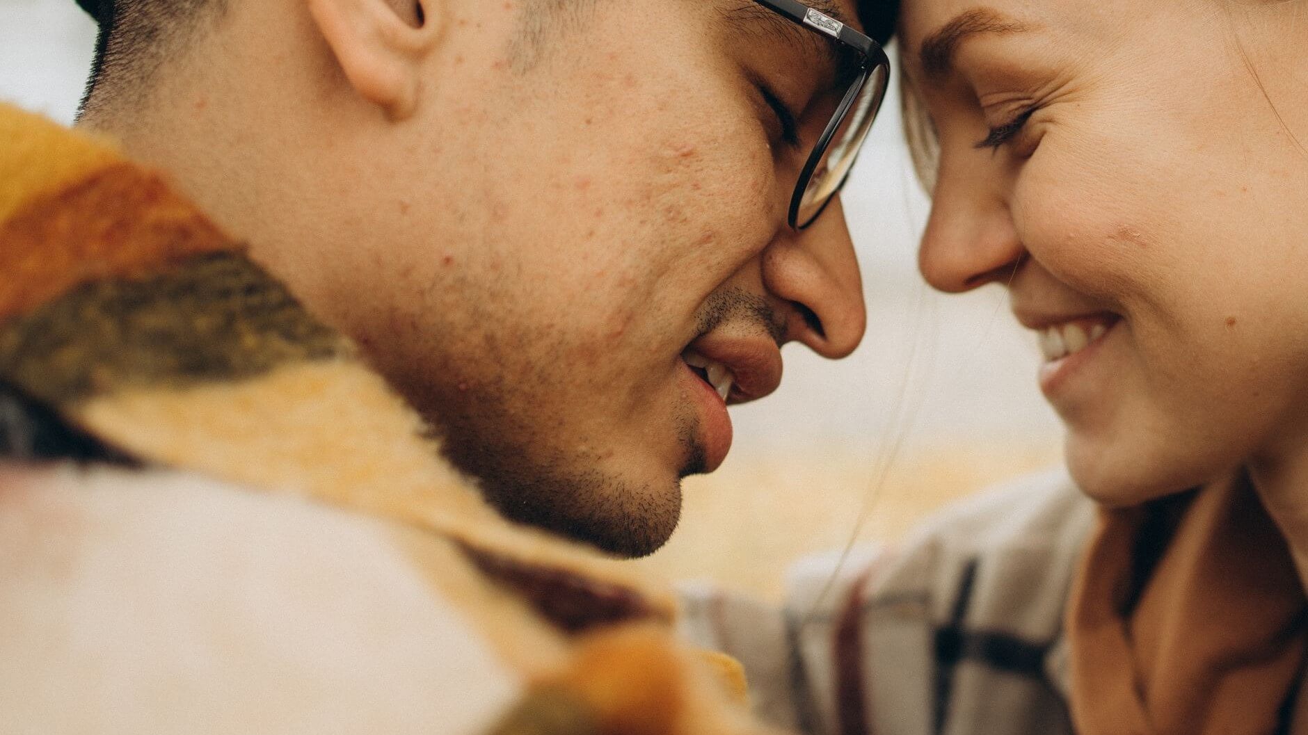 close up of a smiling man and woman's face in an almost kiss
