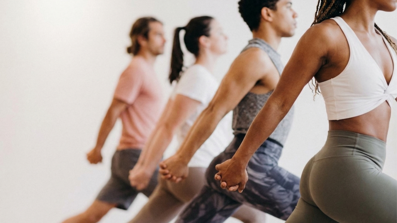A line of four people holding hands and lunging in a yoga class.