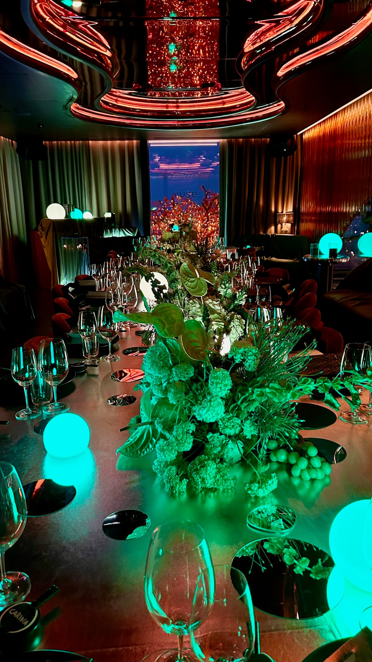 Event design by Amy Lord: a long dinner table with green floral centrepieces and glowing lights under a red neon ceiling