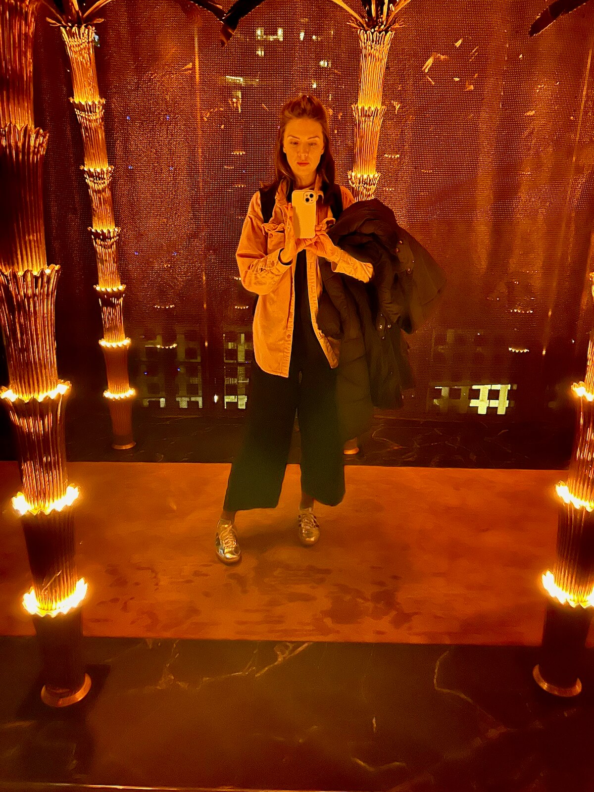 Amy Lord, creative business coach, taking a mirror selfie in a gold-lit room with palm-tree columns