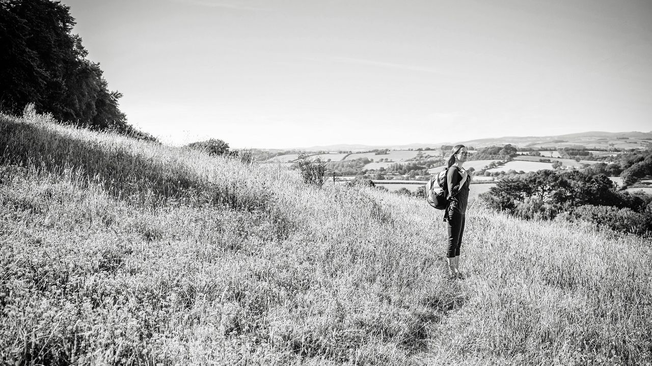 black and white image of a middle-aged woman standing on hill looking over landscape below