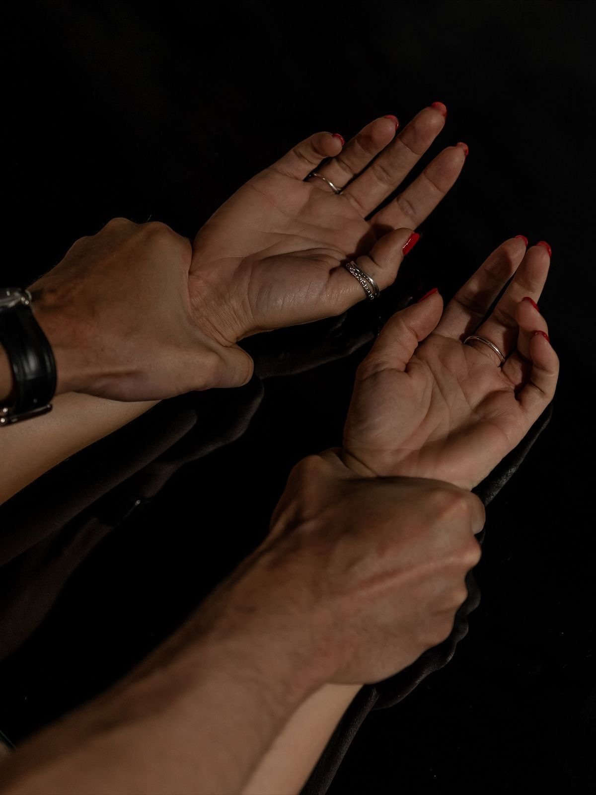 A man's hands gently holding a woman's wrists against a dark background