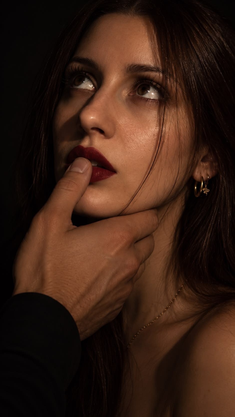 A woman with red lips gazes up at her man as his hand cradles her jaw and his thumb traces her lower lip