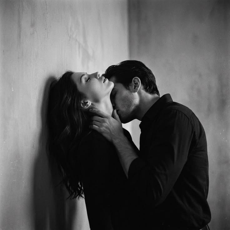 Black and white photograph of a woman leaning back against a wall, eyes closed, as a man in a dark shirt cradles her jaw and kisses her