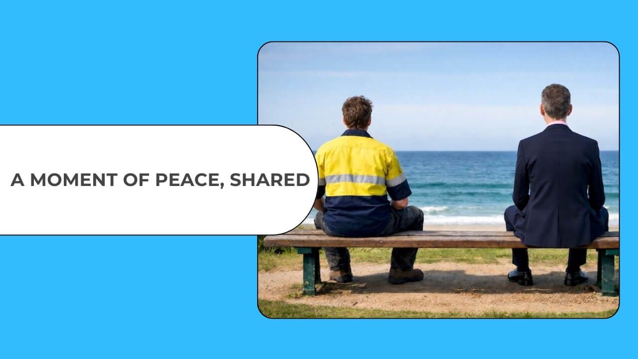 Two men, one in a hi-vis work shirt, the other in a suit, sit side by side on a bench facing the ocean, quietly sharing a peaceful moment.