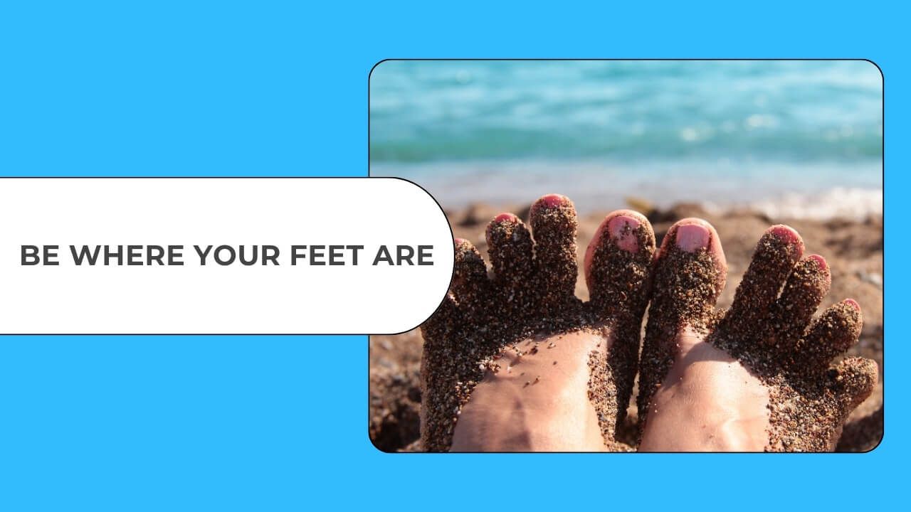 Feet covered in sand at the beach, reminding us to be present in the moment.