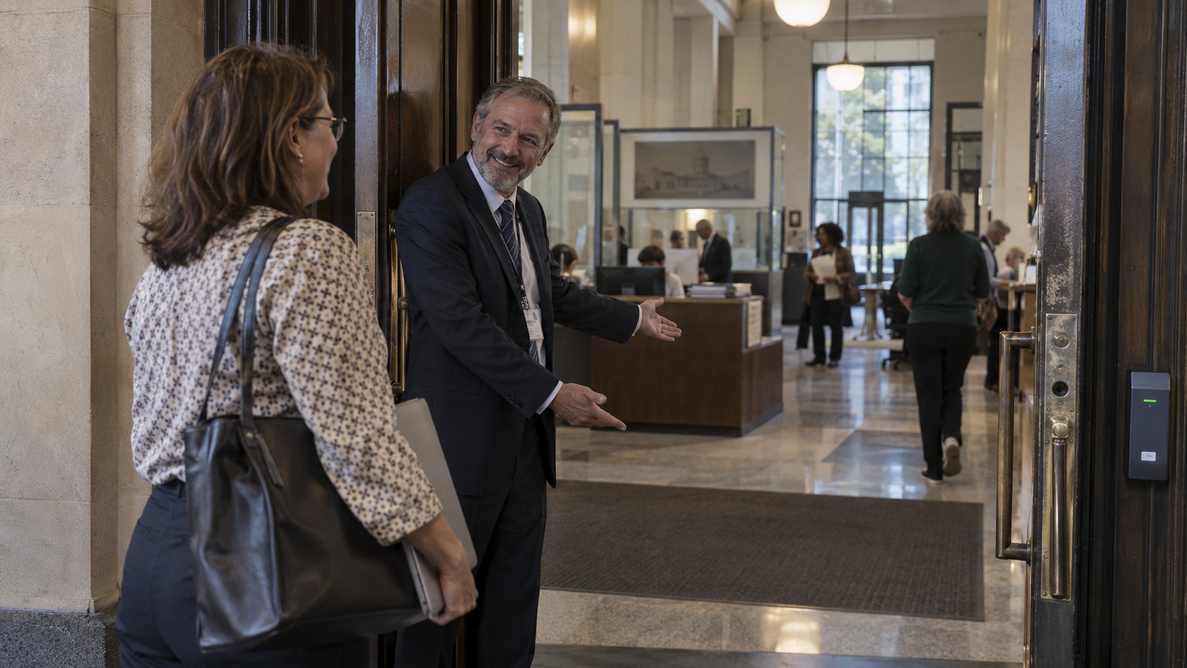 Devant un édifice institutionnel, une personne ouvre la porte d'entrée et accueille chaleureusement une professionnelle qui s'apprête à franchir le seuil.