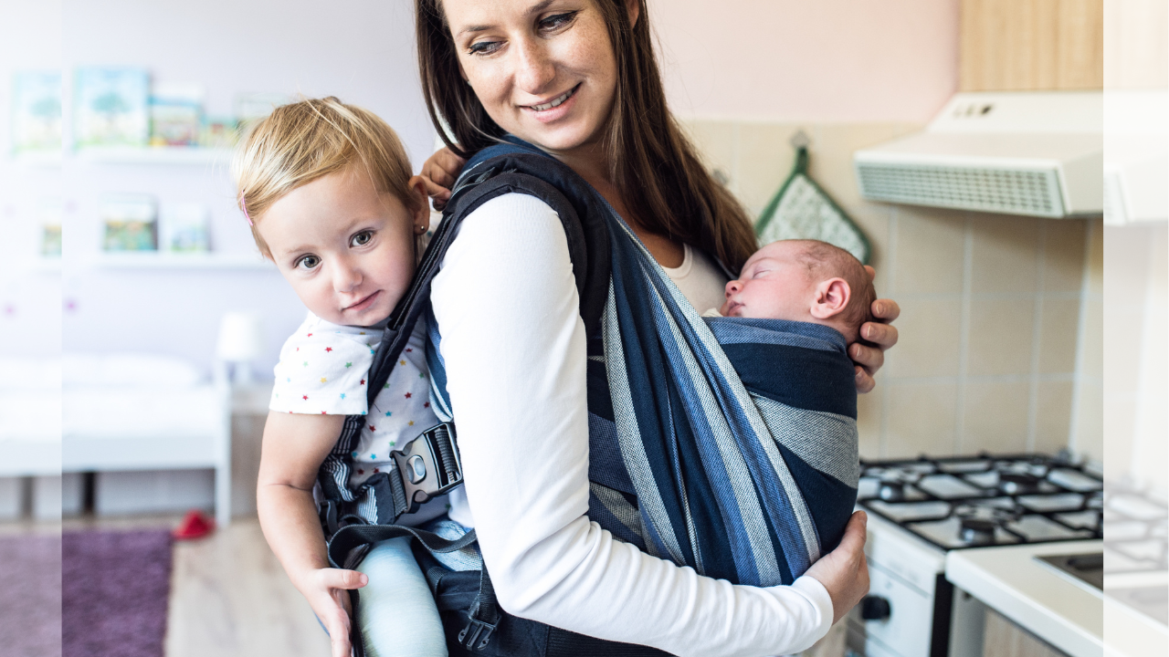 Mother using a wrap carrier for a newborn in front and a soft structured carrier for a toddler on her back, demonstrating safe babywearing techniques.