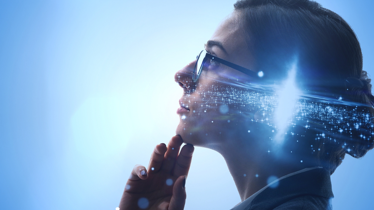 A woman wearing glasses, her hair in a bun, is staring off into space against a blue background while a superimposed picture of a galaxy against her temple implies a rich inner imagination. 