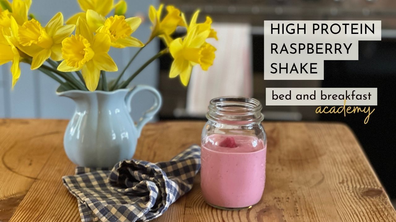 Pink raspberry shake in a mason jar on kitchen table with a jug of daffodils