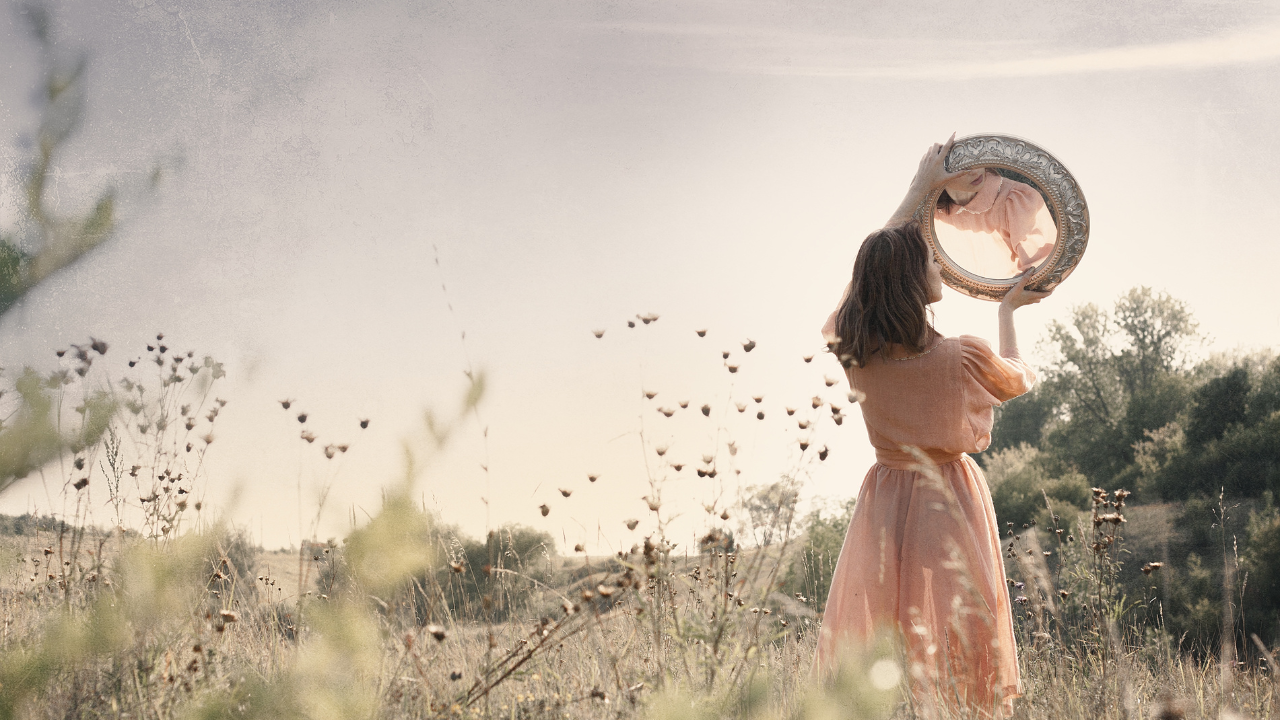 woman in field looking at mirror