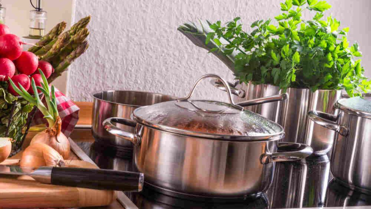 Stainless steel pots cooking on the stove pictured next to an assortment of vegetables including radishes, onions, and asparagus.