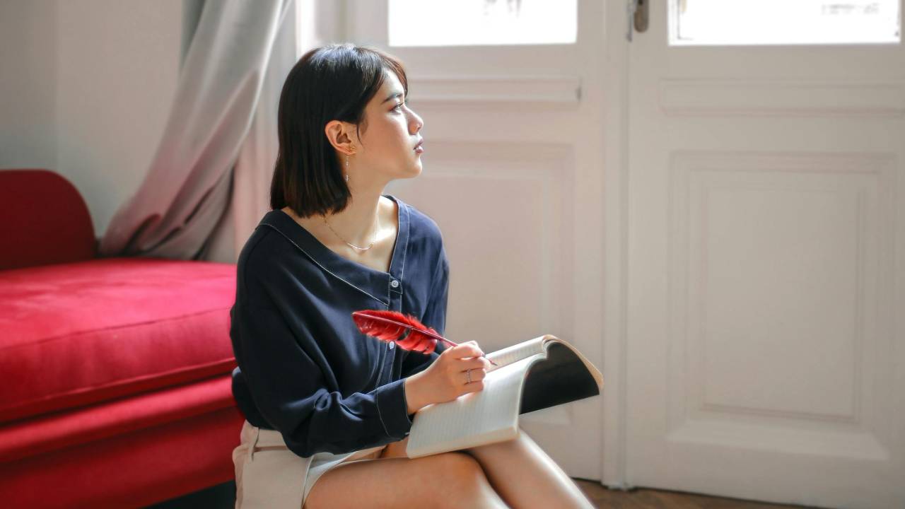 Woman writing with feather pen and staring out the window