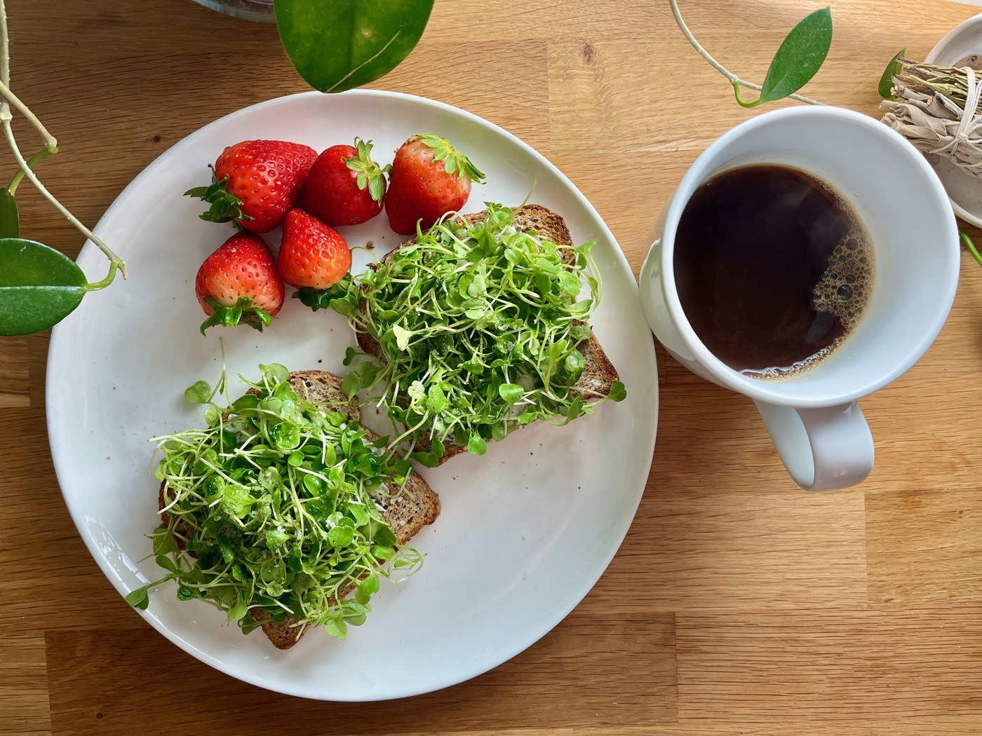 Strawberries beside toast topped with greens and a cup of coffee
