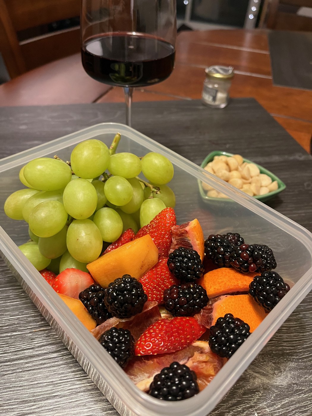 Grapes, strawberries, blackberries, and citrus in a sharing container, with a wine glass behind it