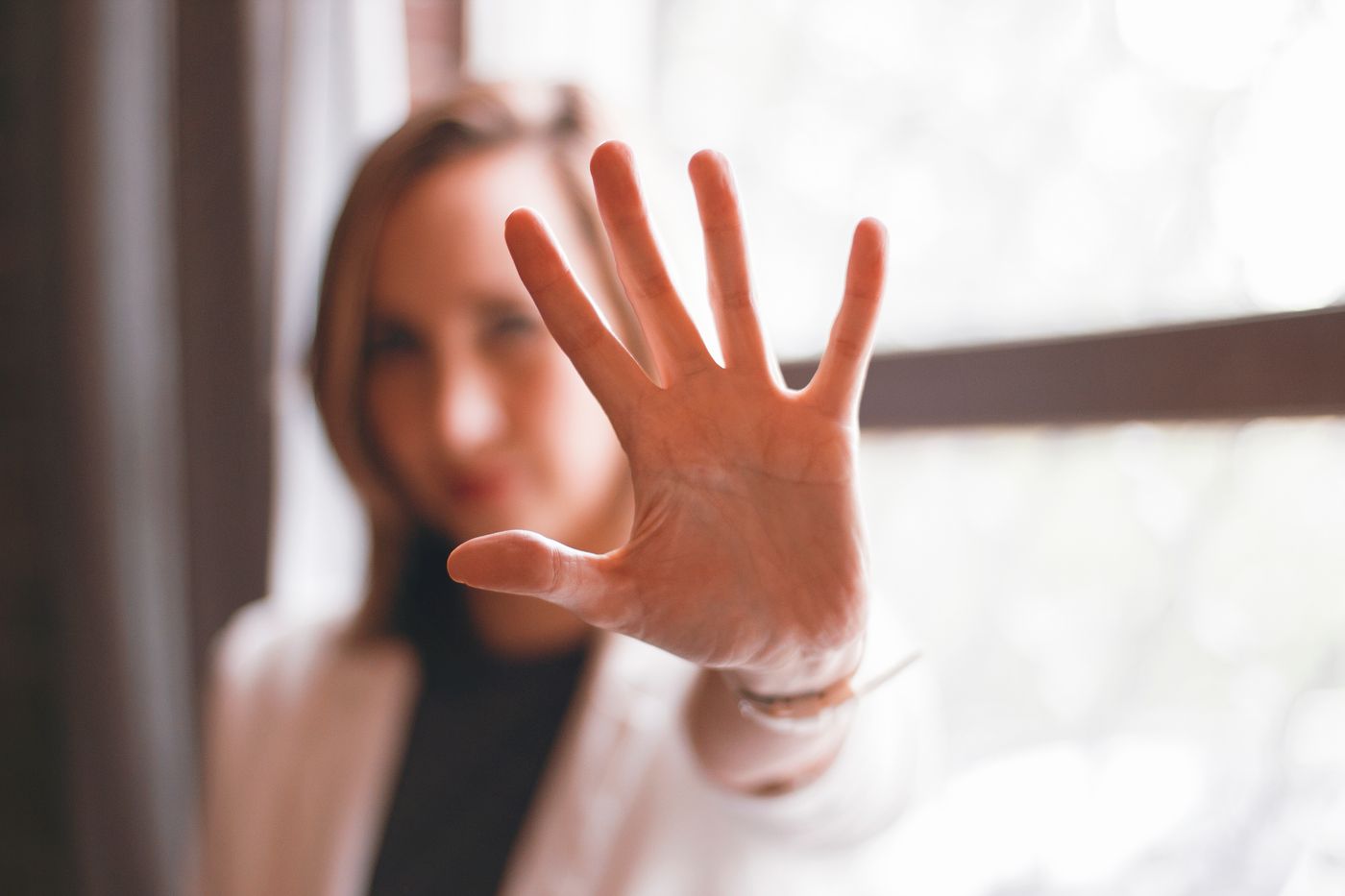 Woman holding her open palm up towards the camera in a calm stop gesture with her face softly blurred behind it, a simple picture of saying no without needing to explain or apologise