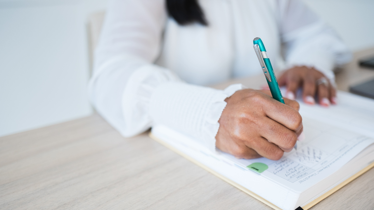 Woman journaling by a window in morning light, reflecting on goals and priorities at the start of a new year.