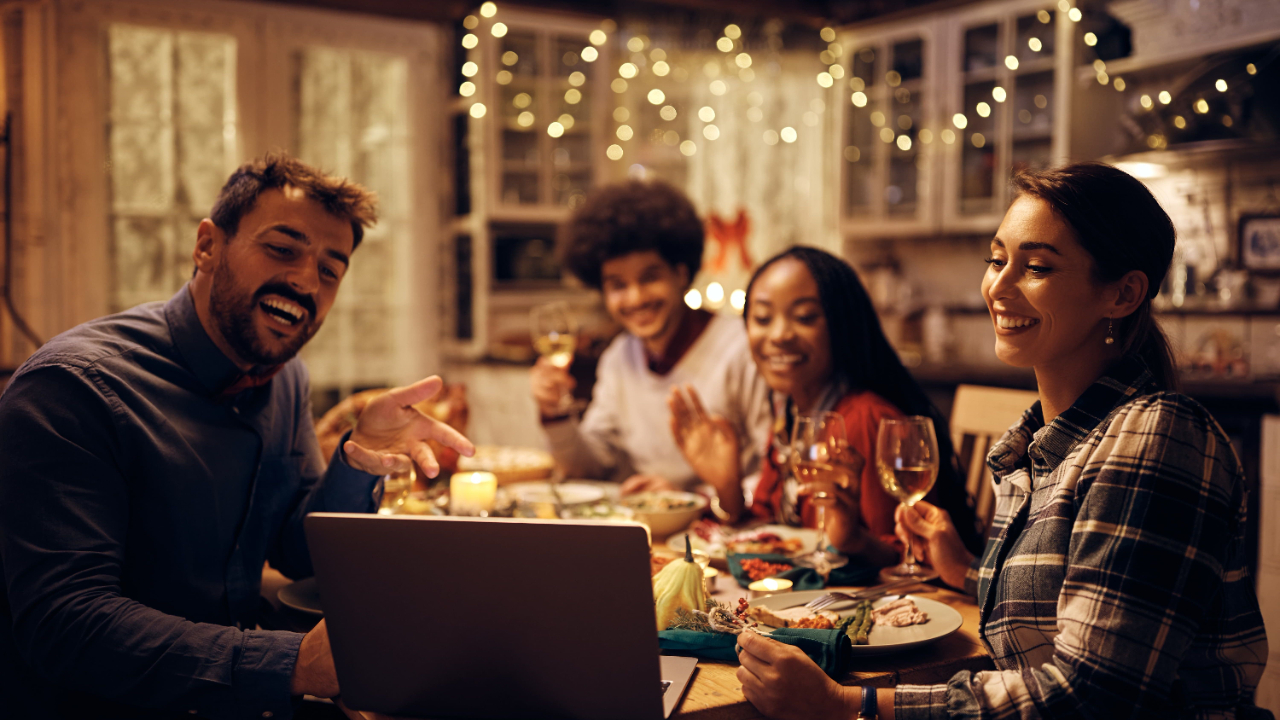 a family shares a thanksgiving meal, connecting with others using their laptop at the table