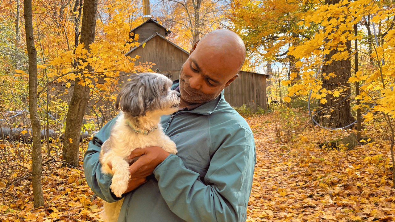 Ivan holding the family pet, a shih tzu named Daisy in the forest near his home in front of a sugar shack.