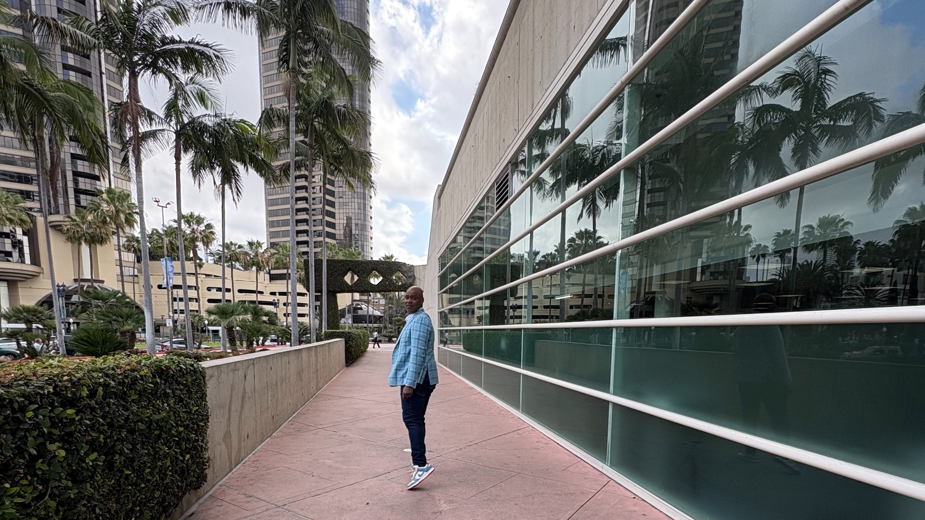 Ivan at a convention in San Diego walking along the sidewalk framed by tall glass buildings and palm trees.