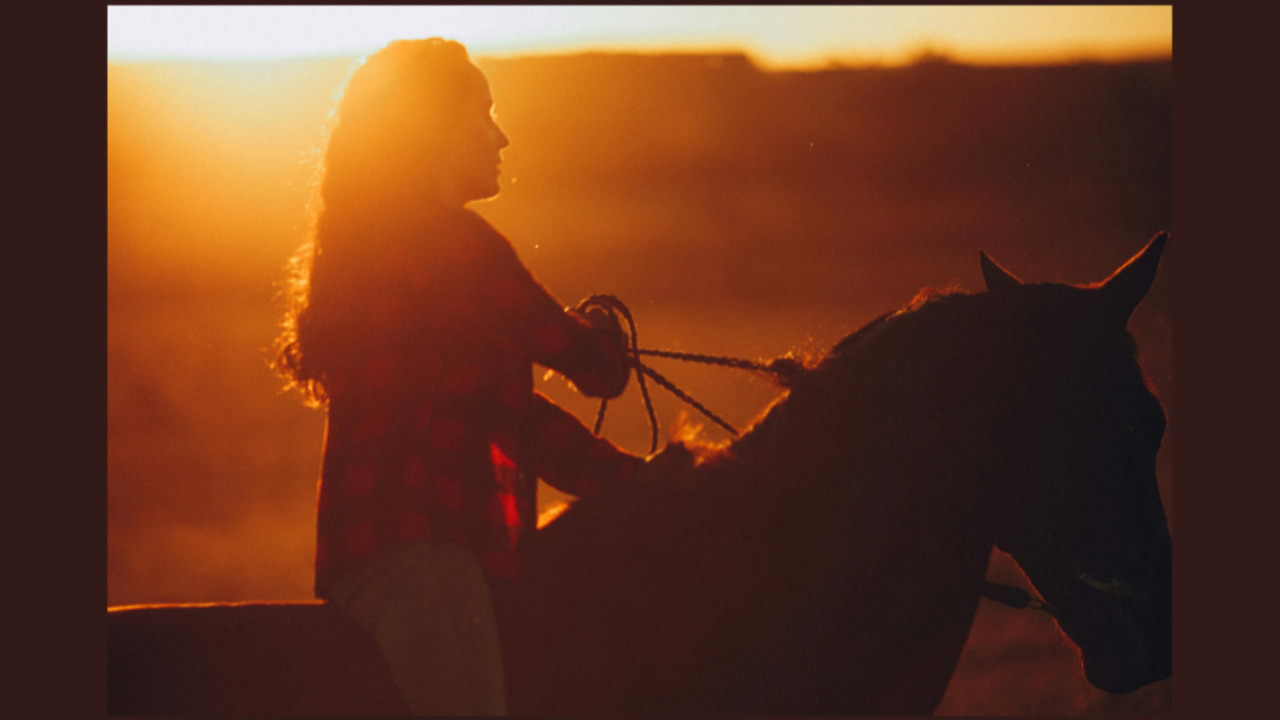 woman with long hair riding a horse with sunset in background